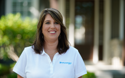 a corporate professional, smiling and standing outside in front of a house in the distance